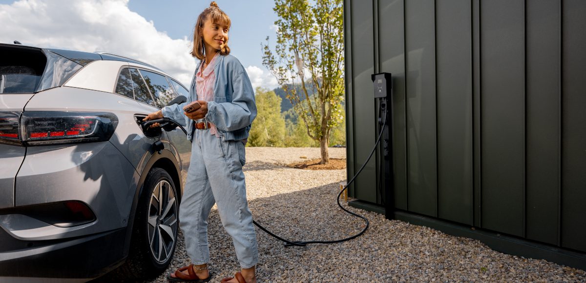 A woman charging an electric vehicle whilst holding her mobile phone